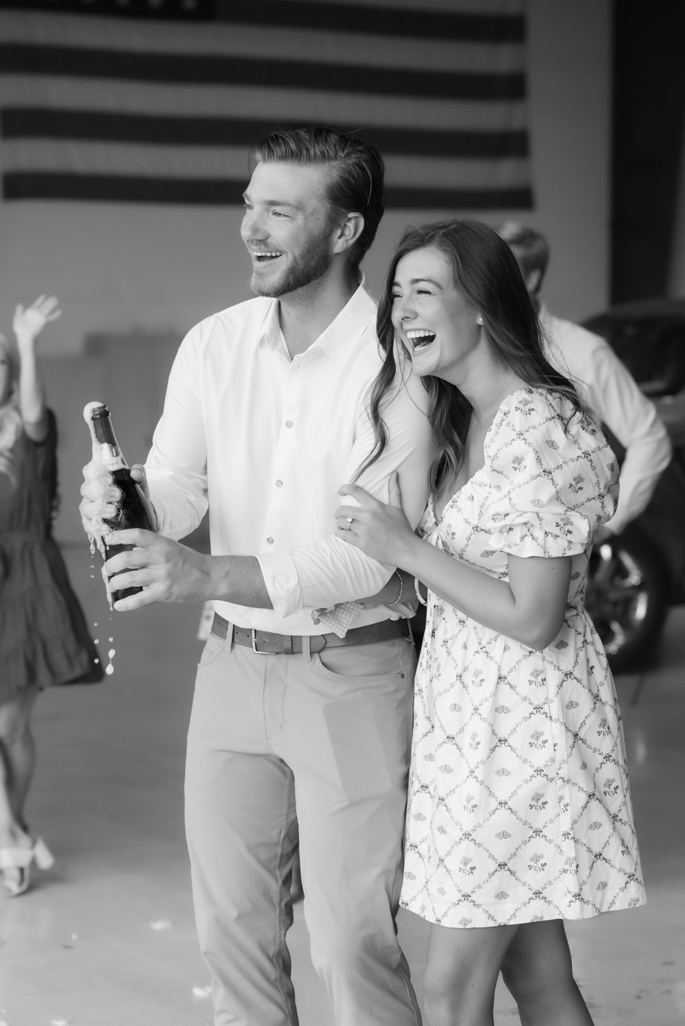 Joyful couple laughing while celebrating at an aviation center with American flag backdrop.