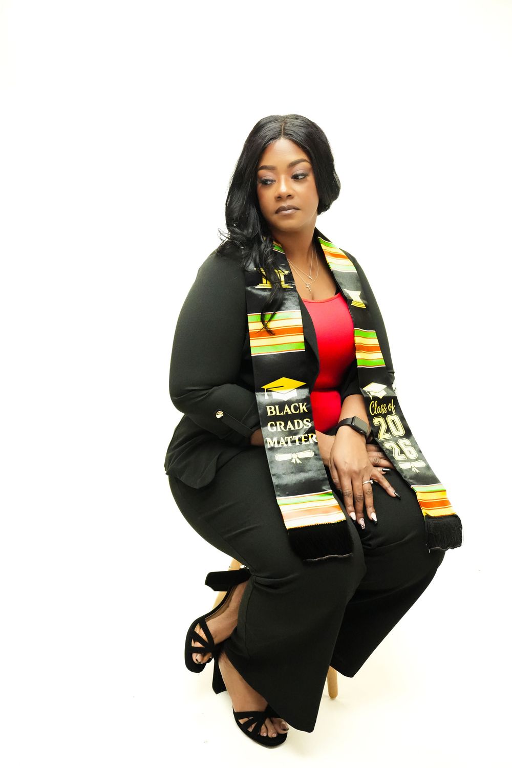 Graduate wearing Black Grads Matter kente stole and cap, seated in professional graduation portrait photo.