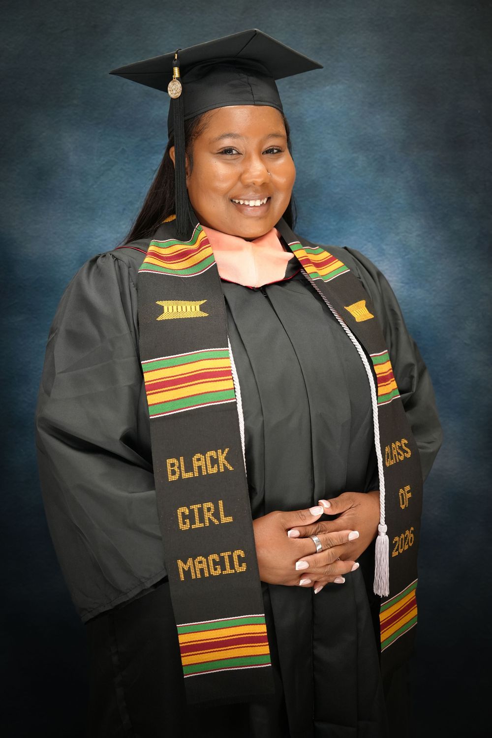 Smiling graduate in black cap and gown wearing a Black Girl Magic kente cloth stole, Class of 2023.