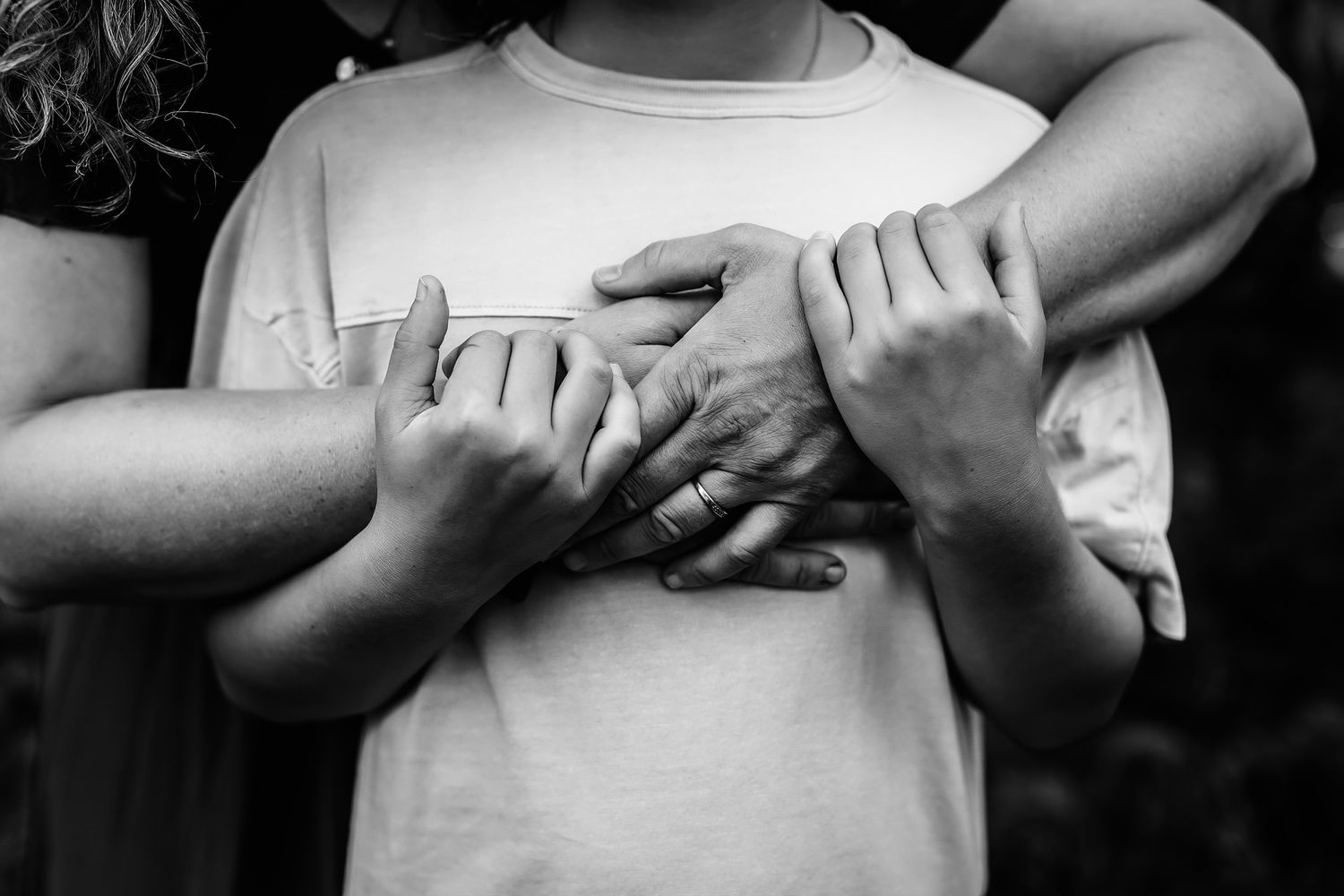 Black and white photo of multiple hands clasped together over a persons chest in a tender embrace.