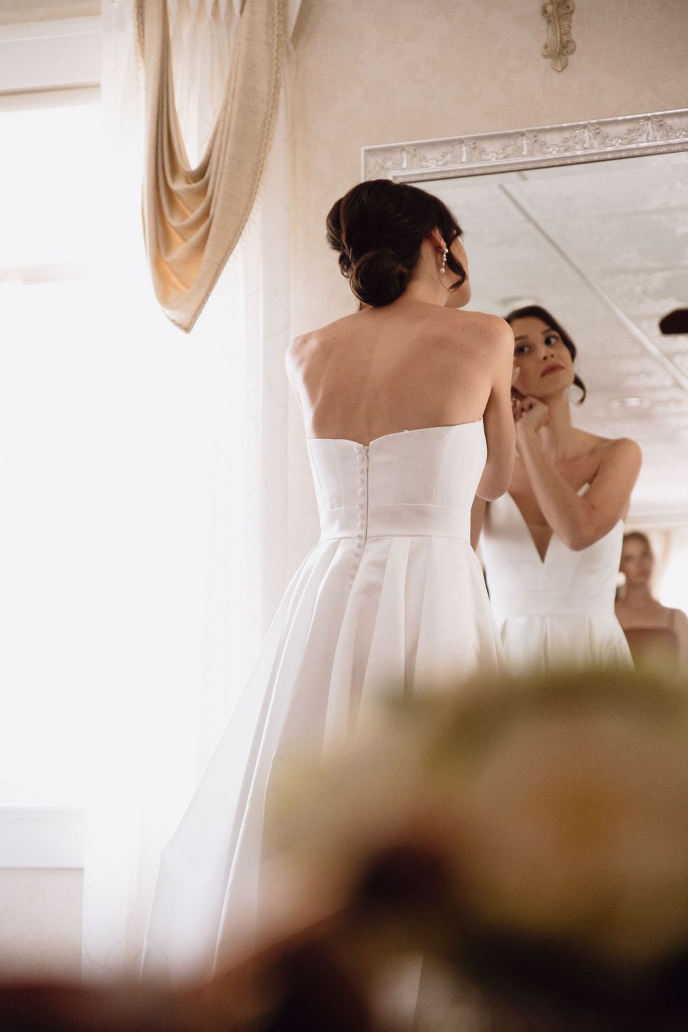A bride in a classic white gown looks at her reflection in an elegant dressing room.