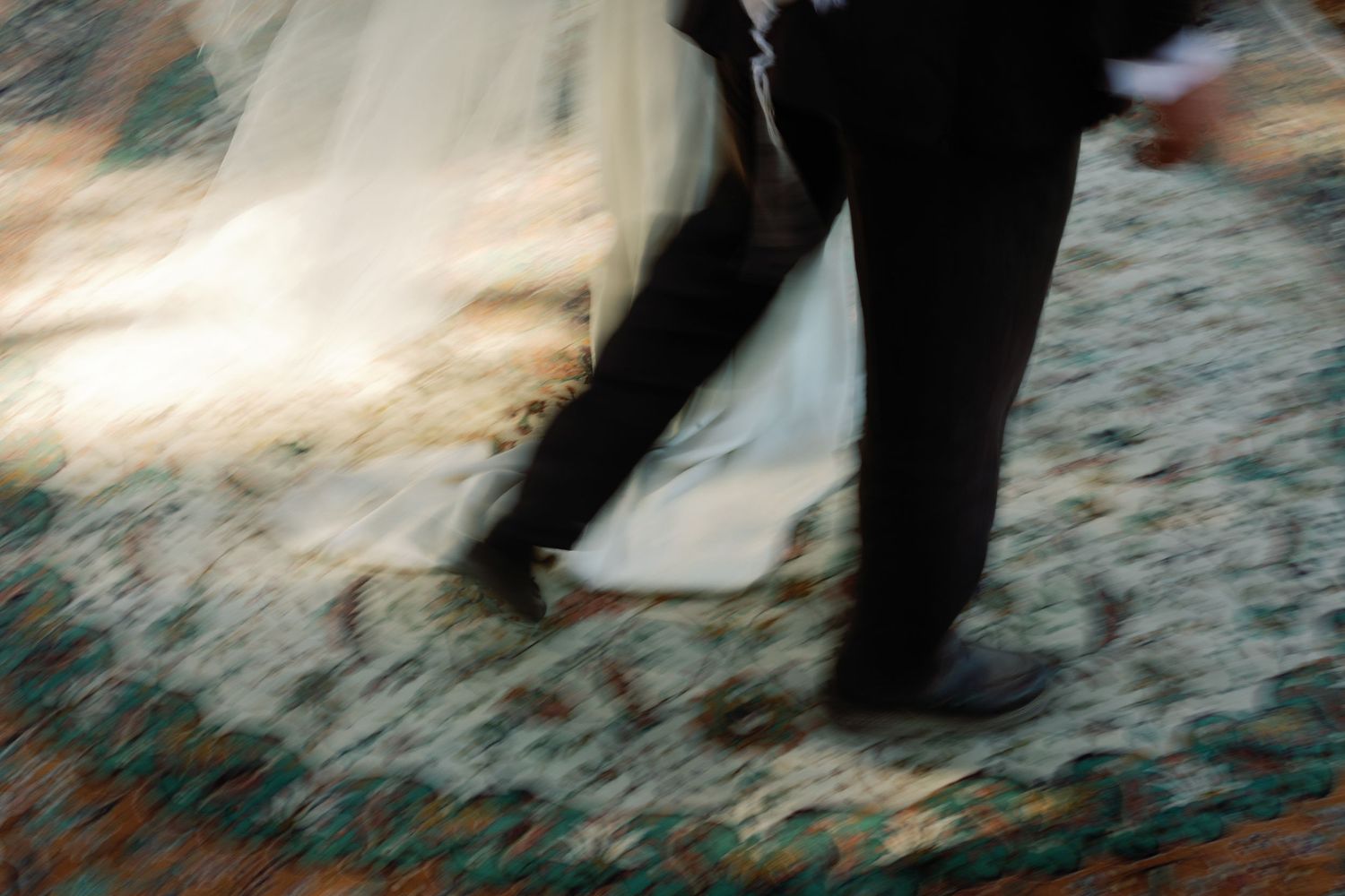 Blurred motion shot of bride and groom dancing at wedding reception on ornate carpet.
