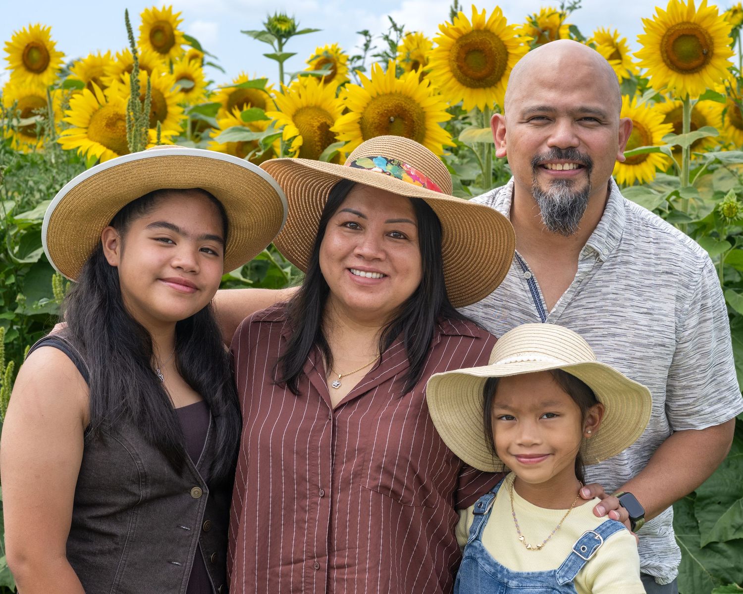 Family of four smiling in a vibrant sunflower field, in the Merrimack Valley for a family photo session