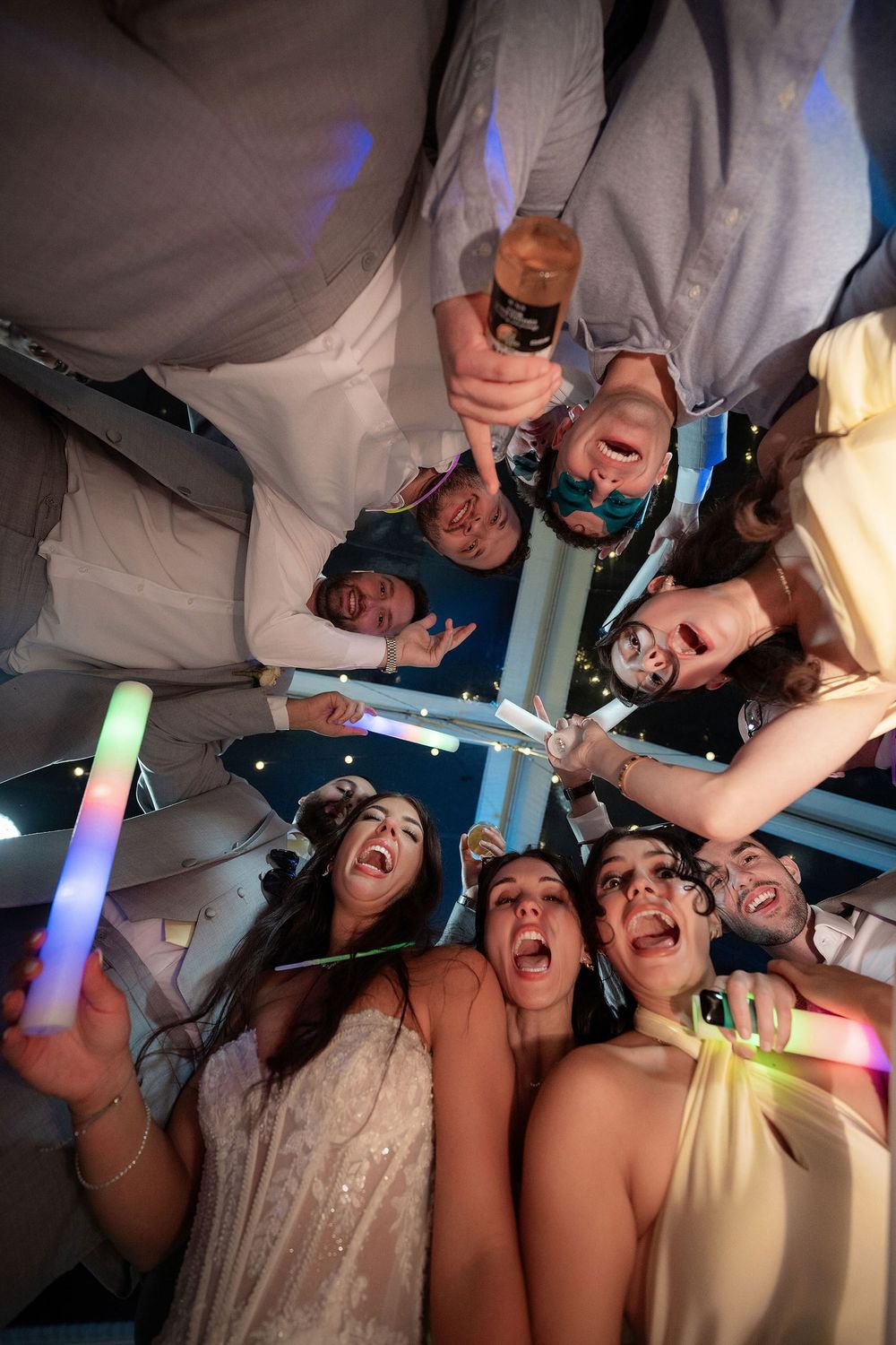 Wedding party huddled together with glow sticks photographed from below at The Mansion at Tuckahoe in Jensen Beach, FL