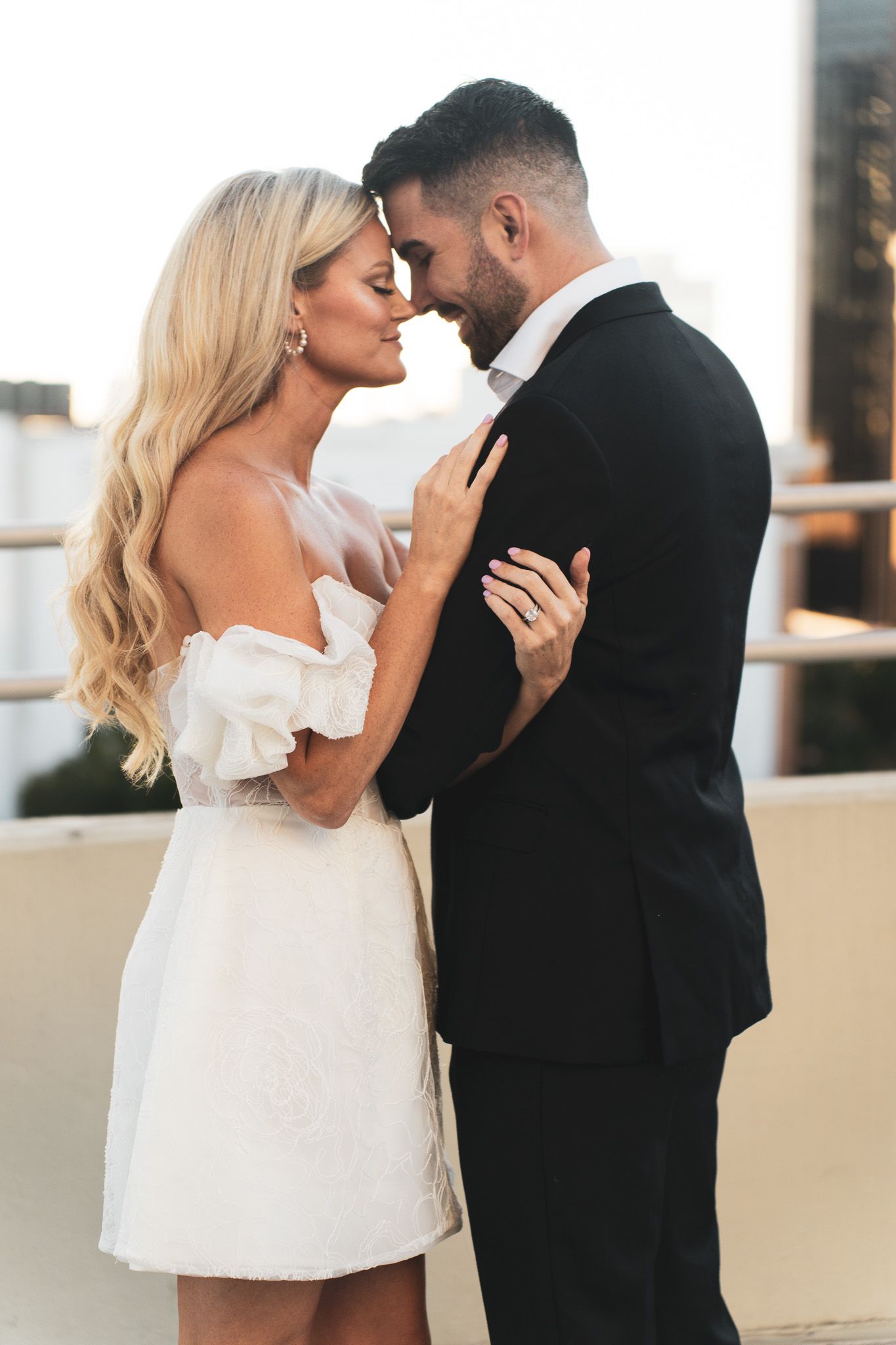 Romantic couple in formal attire sharing an intimate moment on a balcony at sunset.