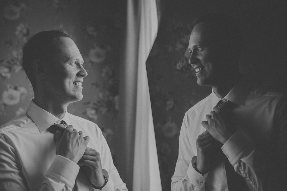 Black and white photo of two grooms adjusting their ties at Gibssons hotel outside Gothenburg