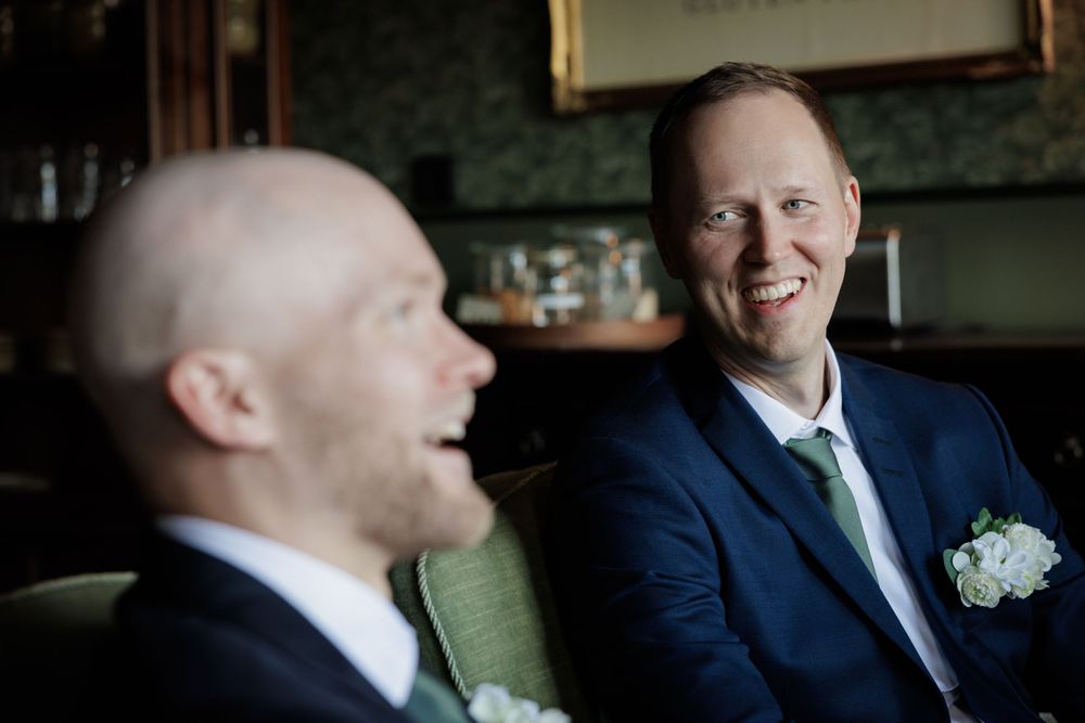 Two grooms in navy suits with white boutonnieres share a joyful moment at their wedding reception.