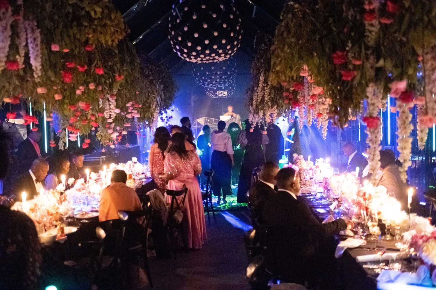 Elegant gala event with floral ceiling decor, disco ball, candlelit tables, and guests in formal attire.