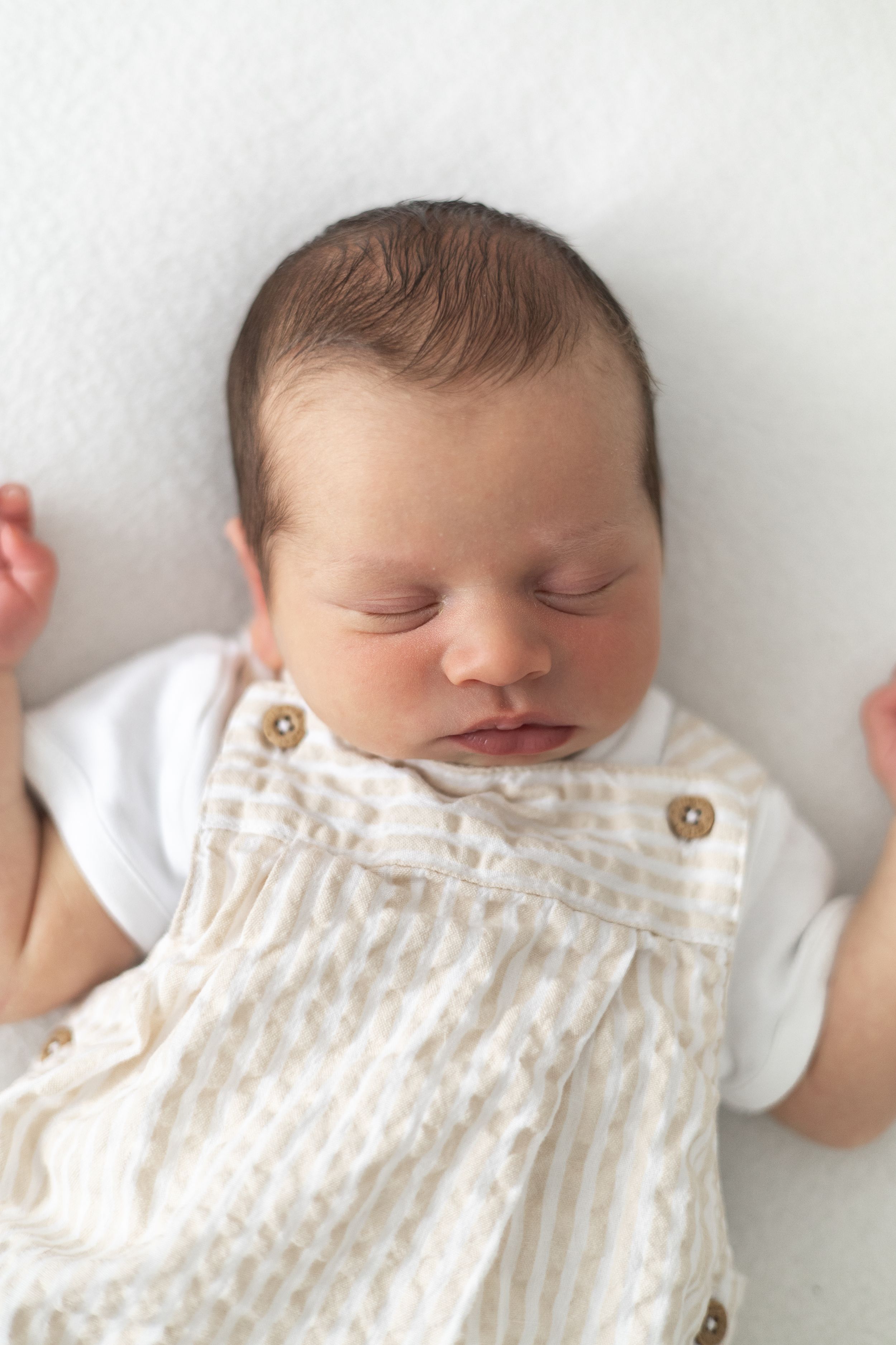 Peaceful newborn baby sleeping on white background wearing striped outfit newborn photoshoot Nottingham