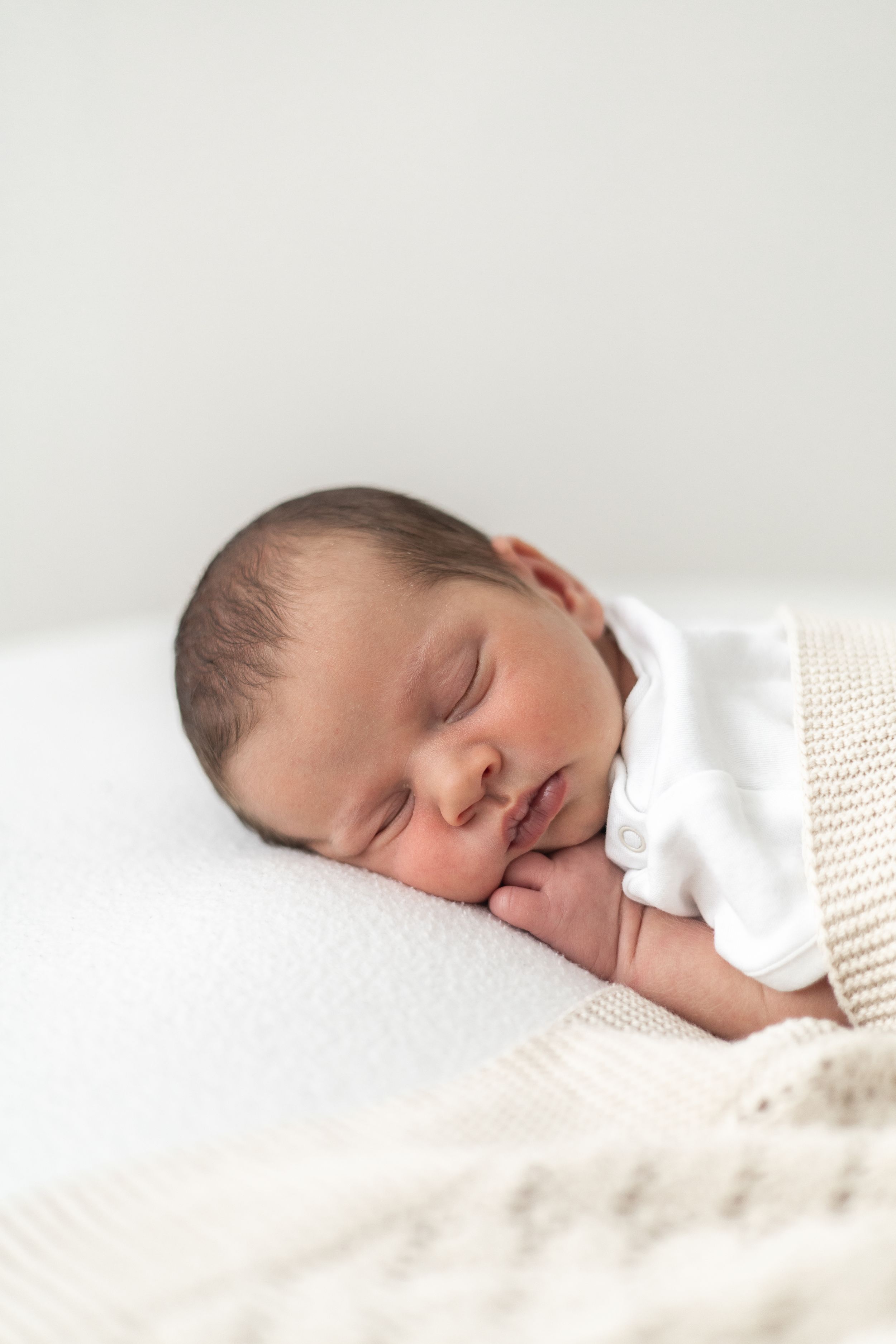 Peaceful newborn baby sleeping on a white pillow, wrapped in a soft cream knit blanket newborn photoshoot Nottingham