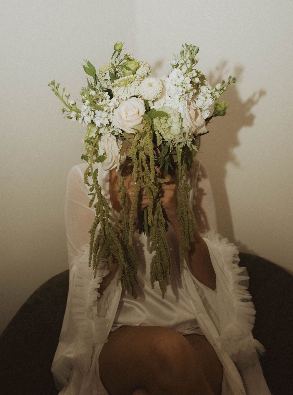 Person wearing an elaborate white floral crown with cascading greenery, dressed in a white gown.