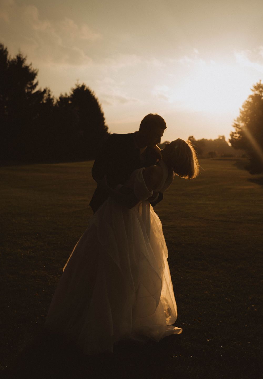 Romantic silhouette of a bride and groom embracing at golden sunset on their wedding day.