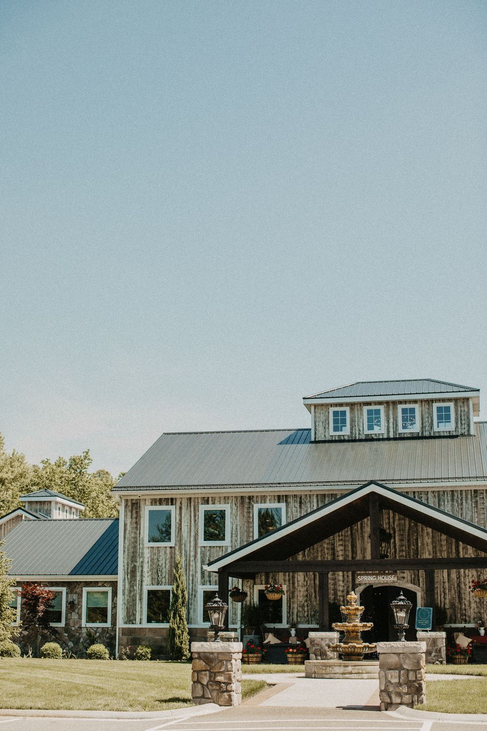 Elegant rustic wedding venue with wood siding, metal roof, and decorative fountain entrance.