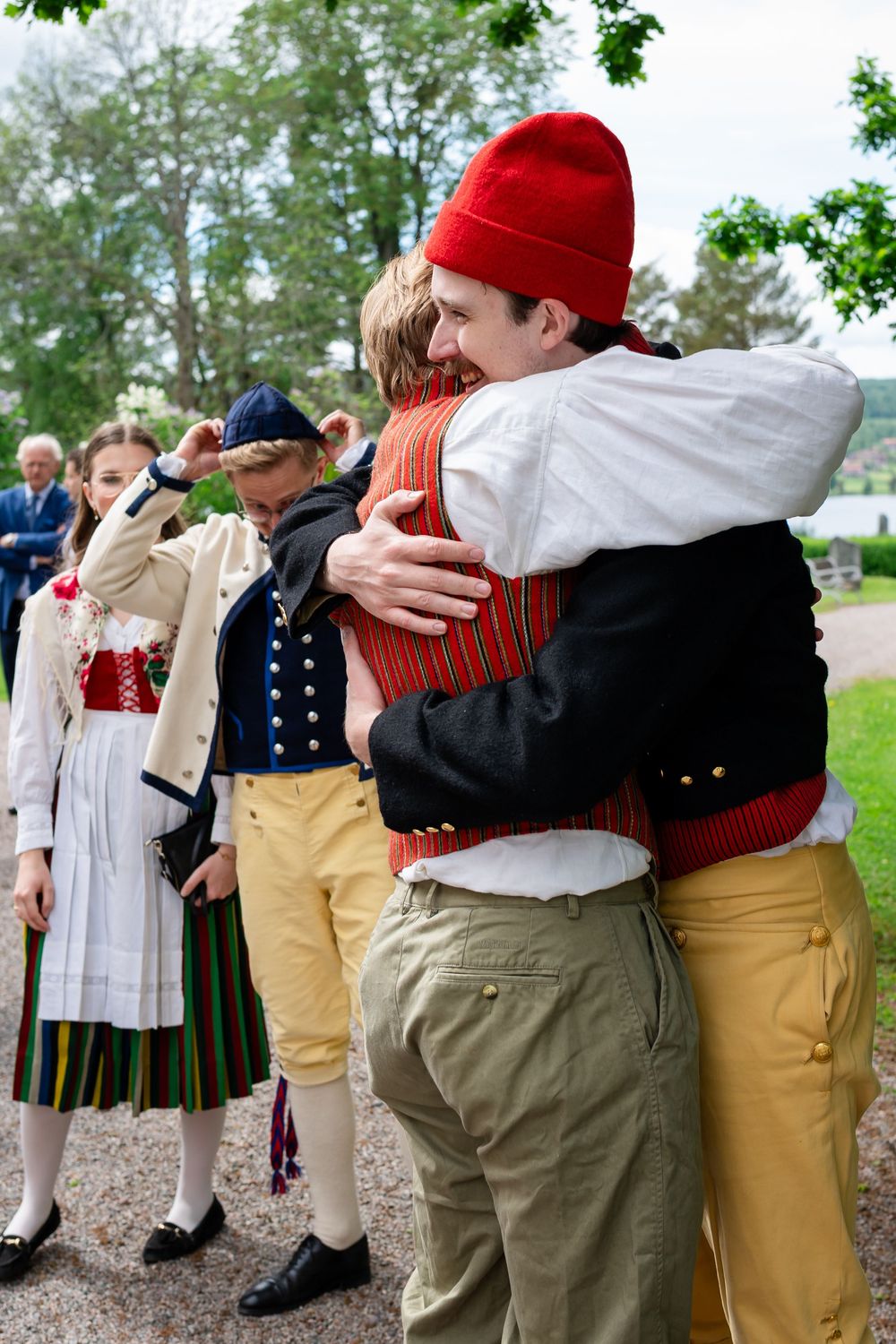 People in traditional Scandinavian folk costumes hugging warmly at an outdoor cultural celebration.