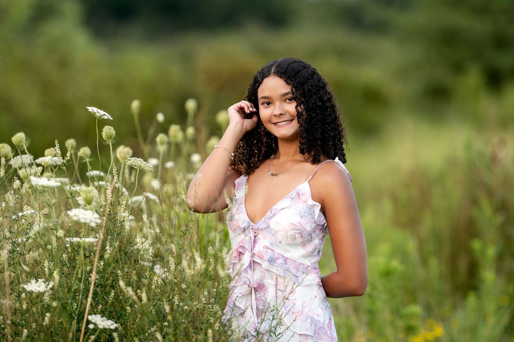 Young woman in floral dress smiling among wildflowers in a lush green field.