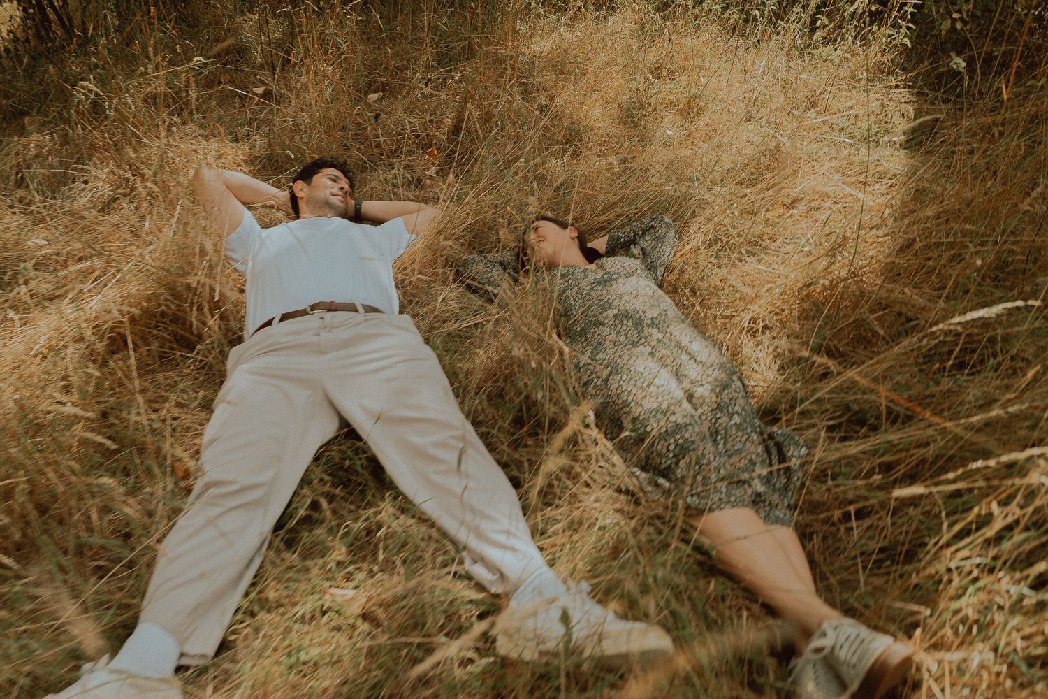 Two people lying relaxed in dry golden grass field, enjoying a peaceful outdoor moment together.