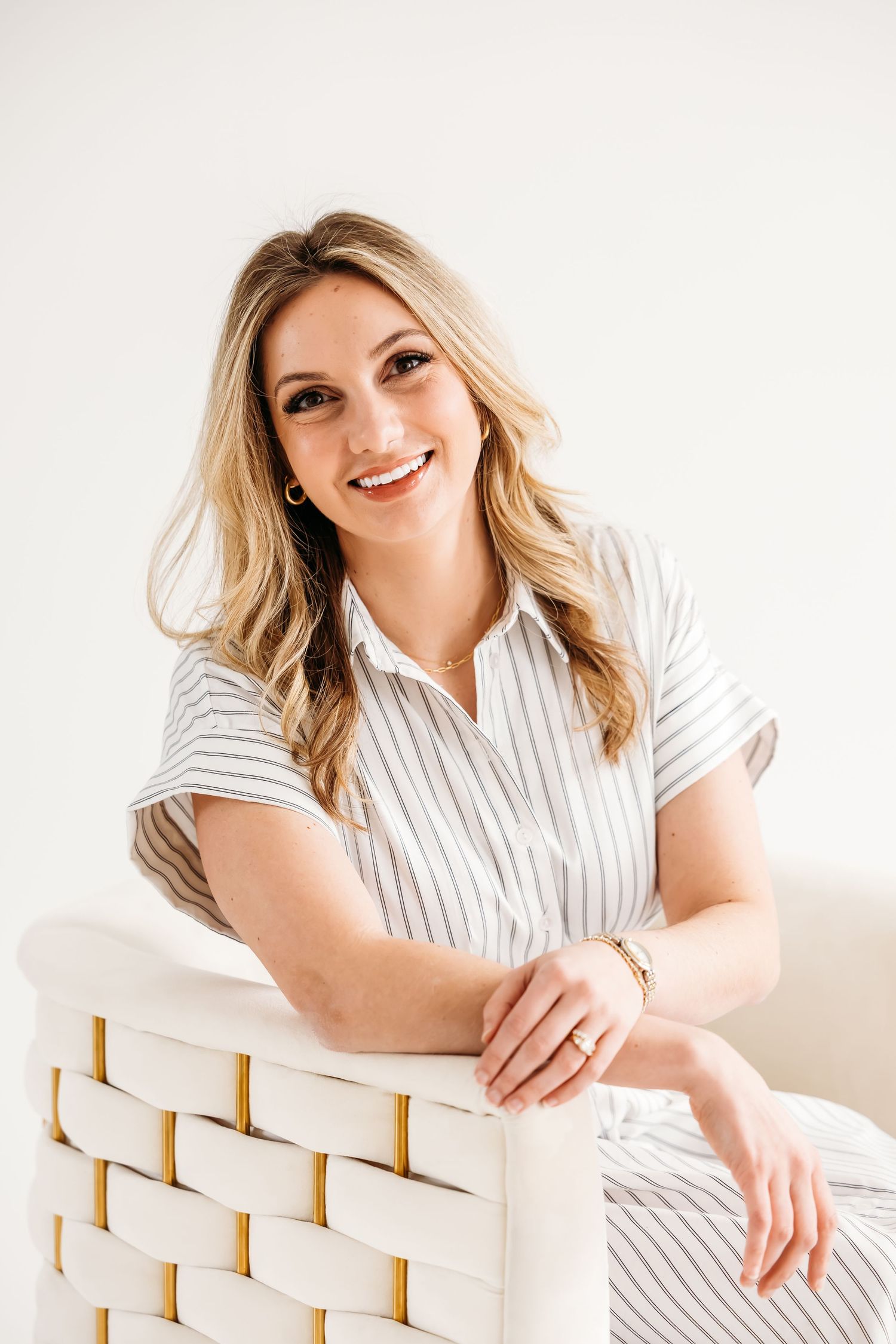 Smiling blonde woman in striped shirt leaning on white woven chair against light background near Yale University in New Haven, CT