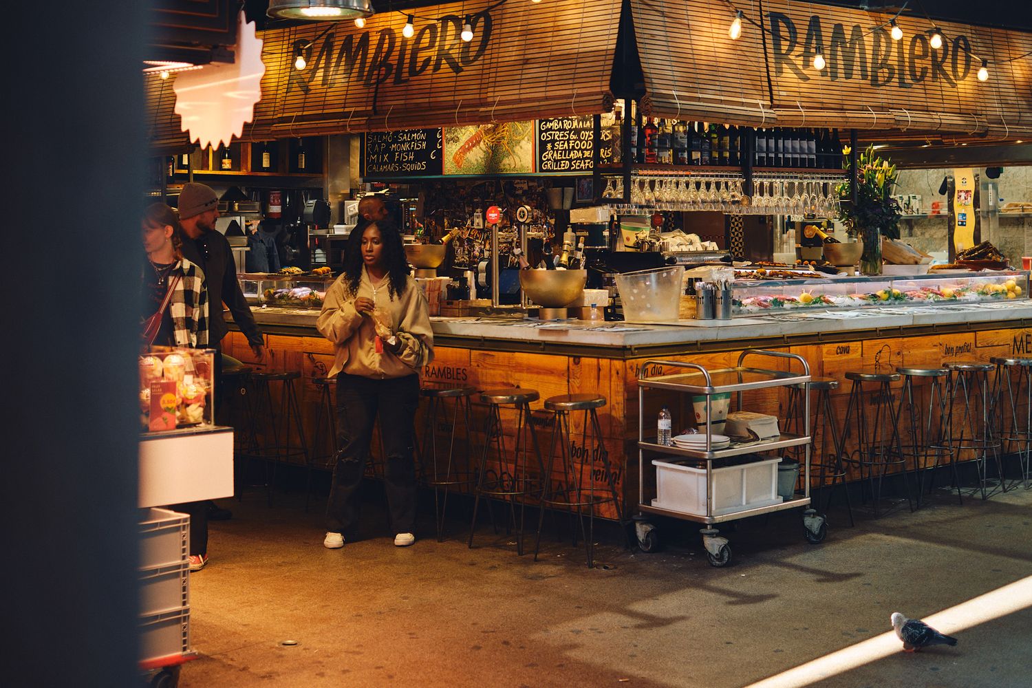 Woman standing at a rustic wooden bar counter inside Rambiero restaurant with warm ambient lighting.