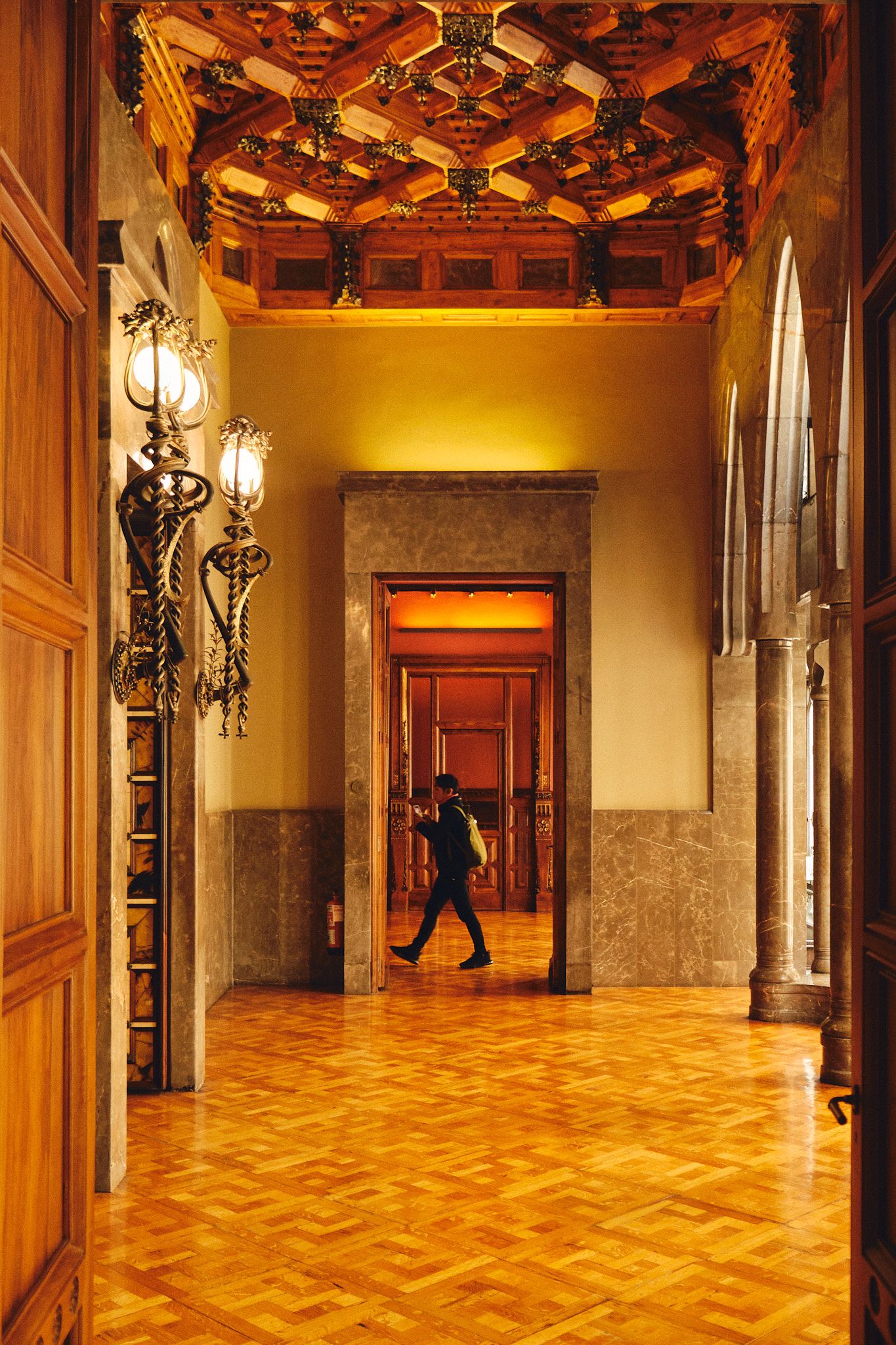 Elegant hallway with ornate wooden ceiling, marble walls, parquet floors, and decorative lanterns in a historic building.