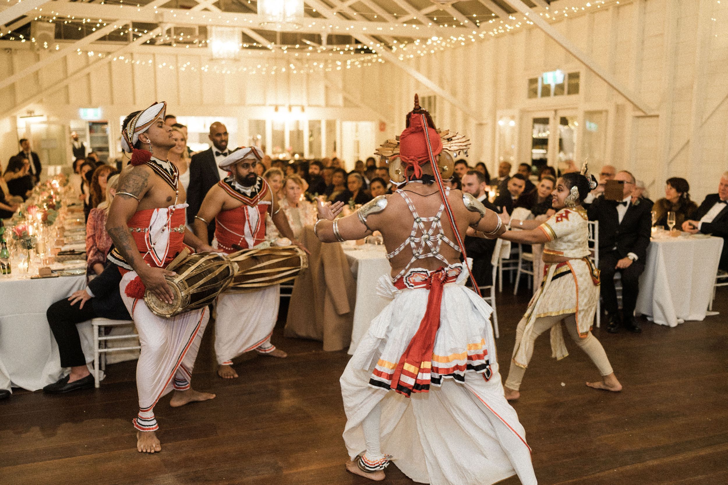 Traditional Sri Lankan Kandyan dancers perform at an elegant wedding reception with string lights and seated guests.