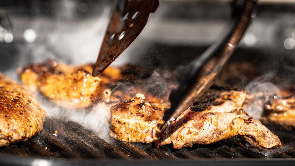 Tongs flipping seasoned grilled chicken pieces on a hot grill with smoke rising, perfect BBQ cooking technique.