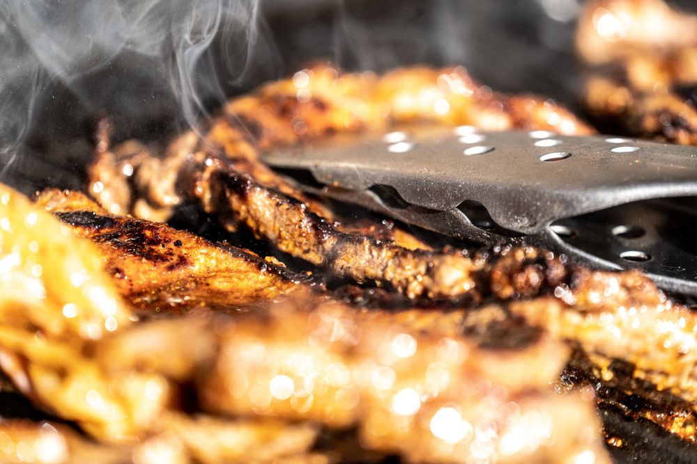 Smoky grilled chicken wings being turned with metal tongs on a hot barbecue grill.