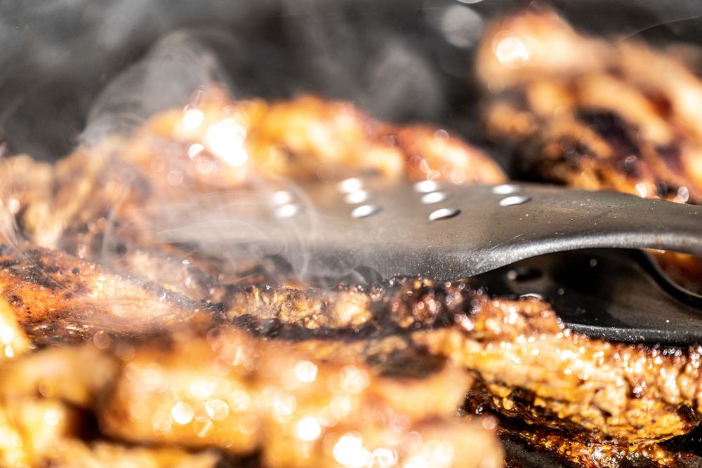 Close-up of smoky grilled meat being handled with metal tongs on a sizzling barbecue grill.