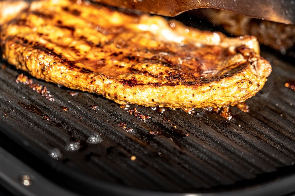 Grilled steak with char marks cooking on a cast iron grill pan, seasoned with spices.