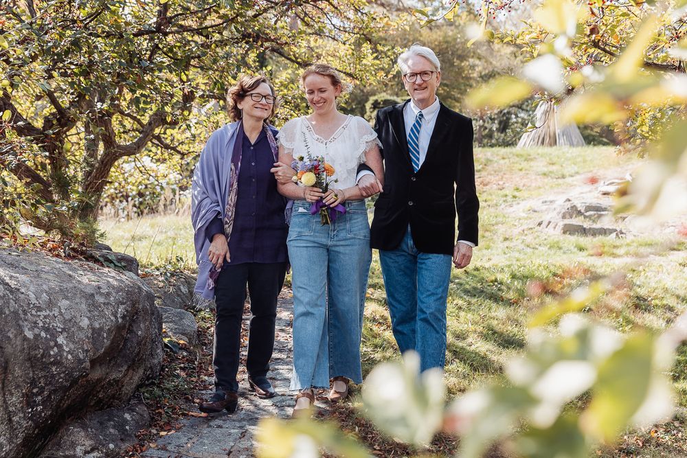 Three people smile while walking on a garden path surrounded by autumn foliage.
