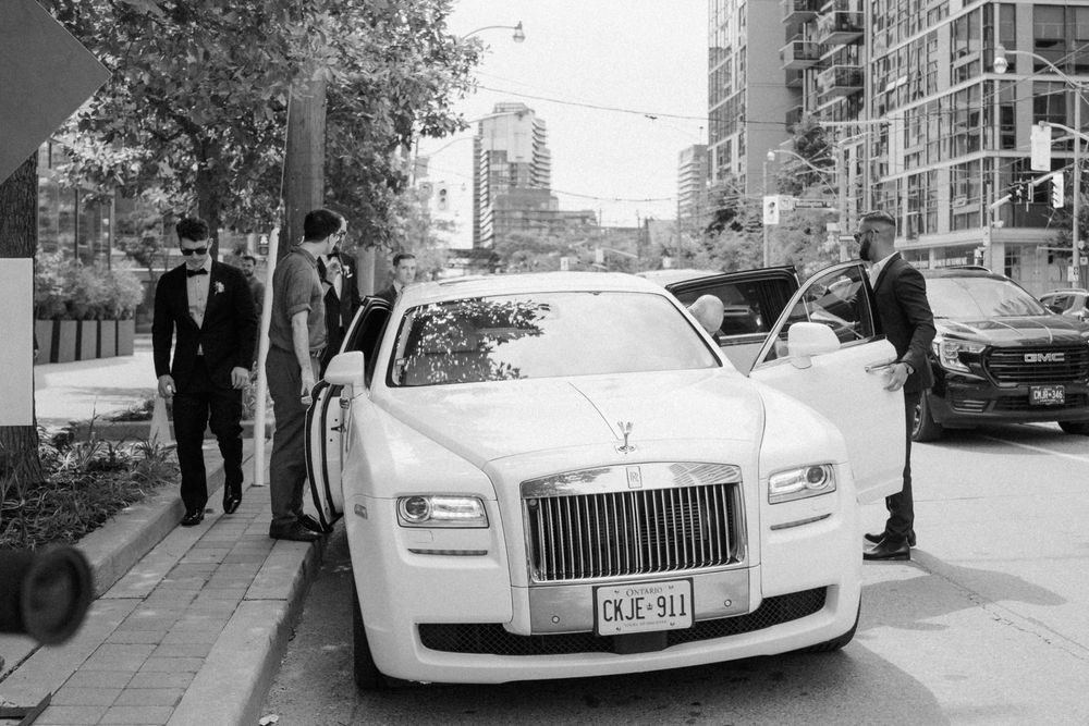White Rolls-Royce wedding car parked on city street with guests in formal attire.
