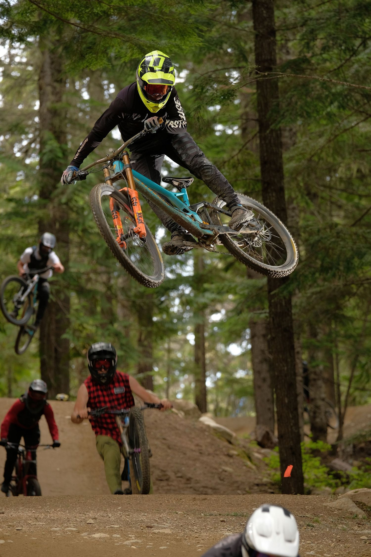 Mountain biker in neon gear performs jump on dirt trail while others watch below.
Whistler Mountain Bike Park
Crankworx
