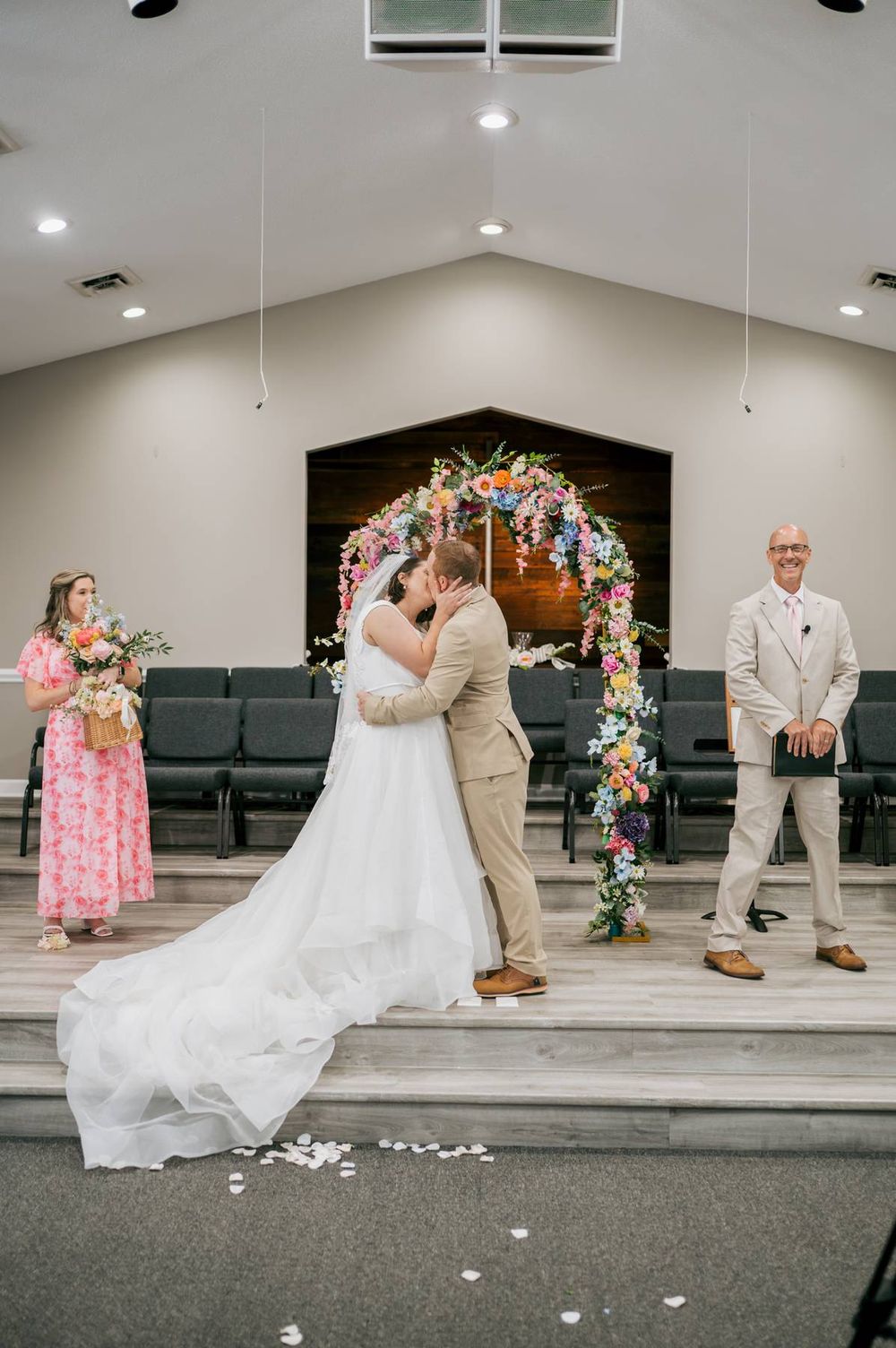 Newlyweds share first kiss at church altar under vibrant colorful floral arch during wedding ceremony, wedding photographer NC