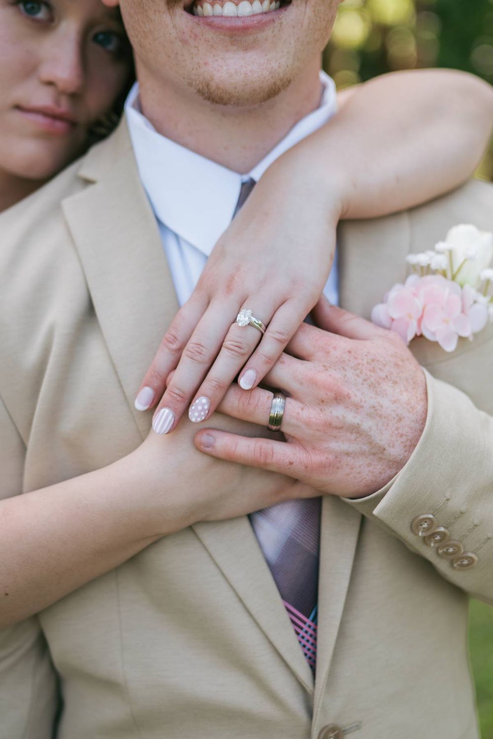 Close-up of bride and groom displaying wedding rings on grooms tan suit jacket outdoors, wedding photographer Asheboro NC