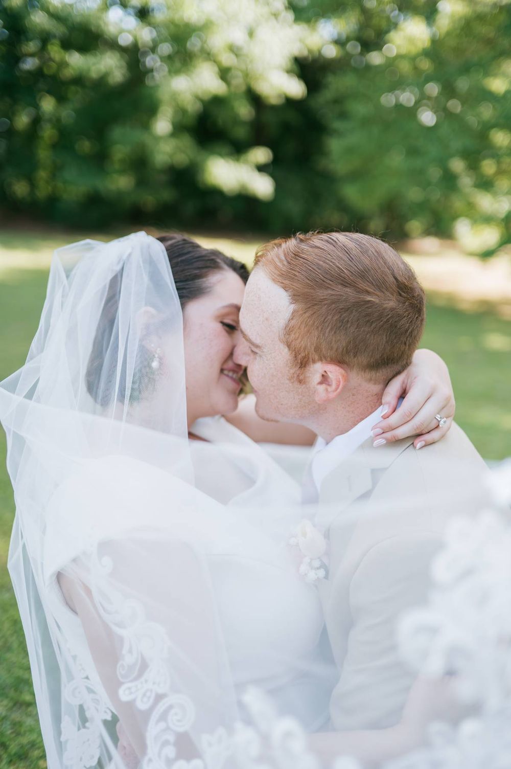 Bride and groom share intimate moment under flowing lace wedding veil in outdoor garden setting, wedding photographer NC
