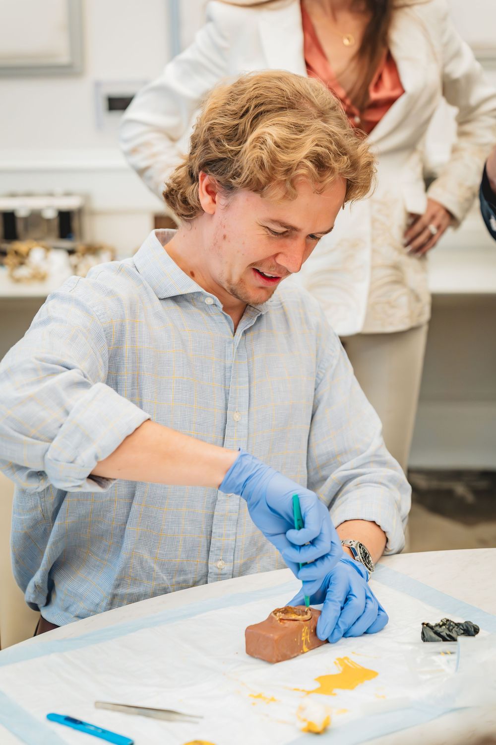 Man in blue shirt and gloves examines artifact on table in laboratory setting.