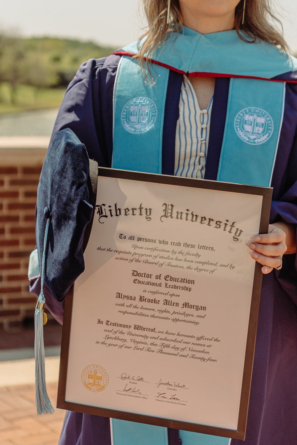 Liberty University Doctor of Education diploma held by a graduate in blue commencement regalia.