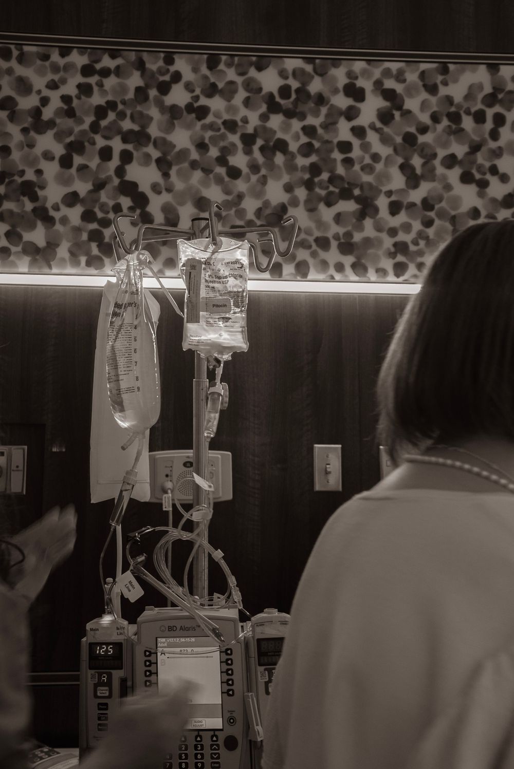 Black-and-white photo of an IV drip stand with medical equipment in a hospital room.