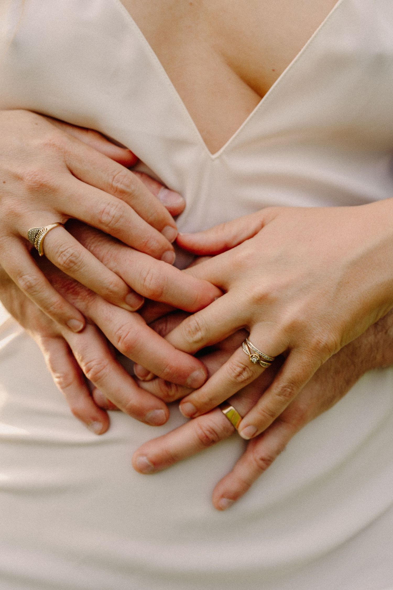 Close-up of two pairs of hands with gold wedding rings intertwined against a white wedding dress.