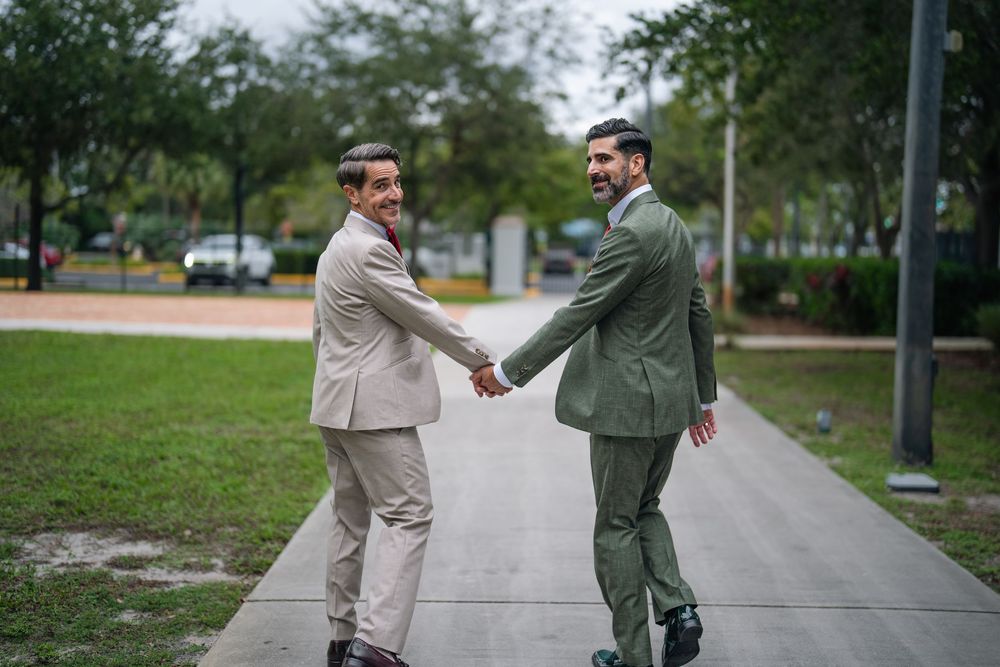 Two businessmen in suits shaking hands on a sidewalk outdoors, smiling in a professional greeting.