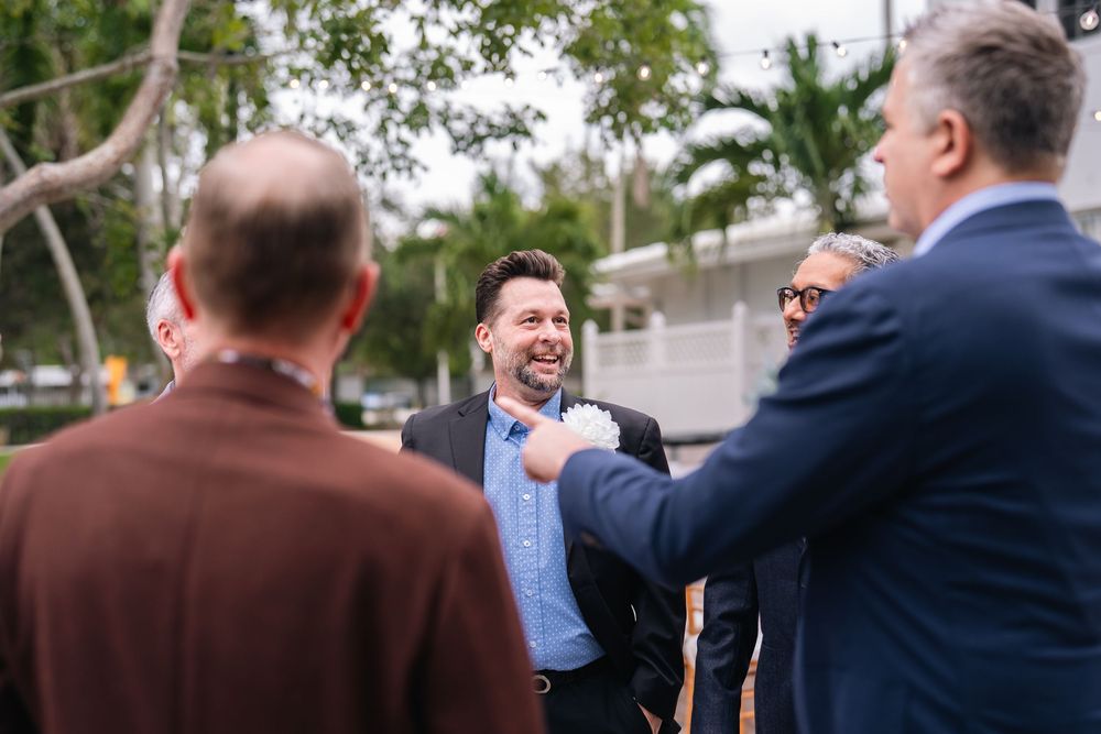 Group of men in business casual attire laughing and socializing outdoors near palm trees at a networking event.