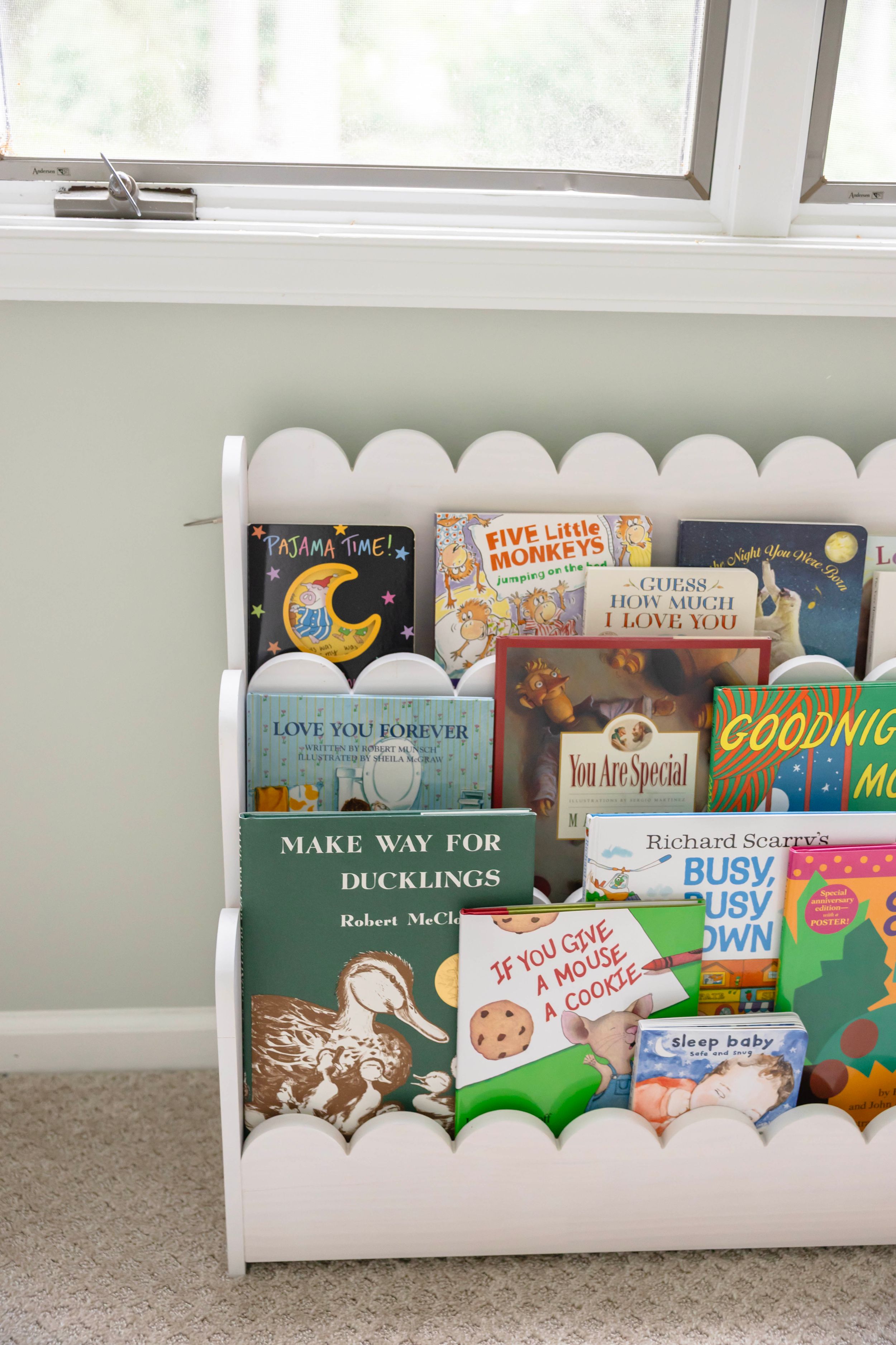 White scalloped children's bookshelf displaying classic kids books including Make Way for Ducklings and Goodnight Moon.
