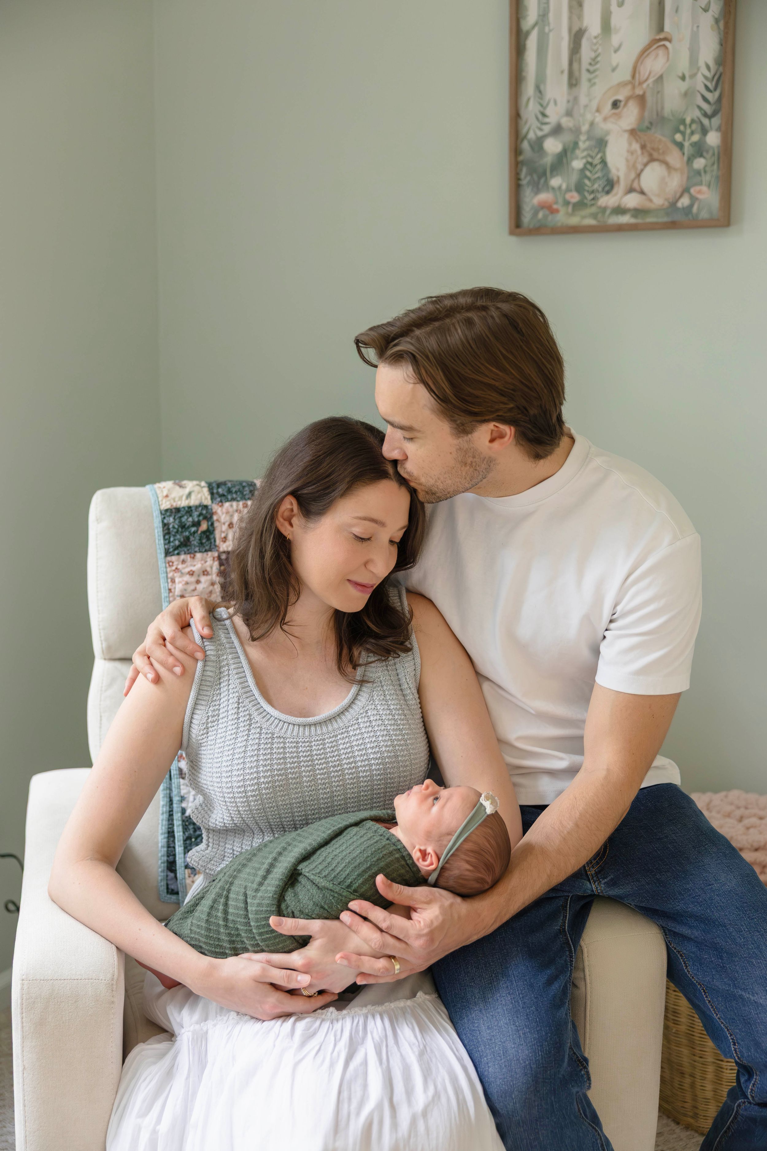 New parents share a tender moment with their swaddled newborn baby in a softly decorated nursery.