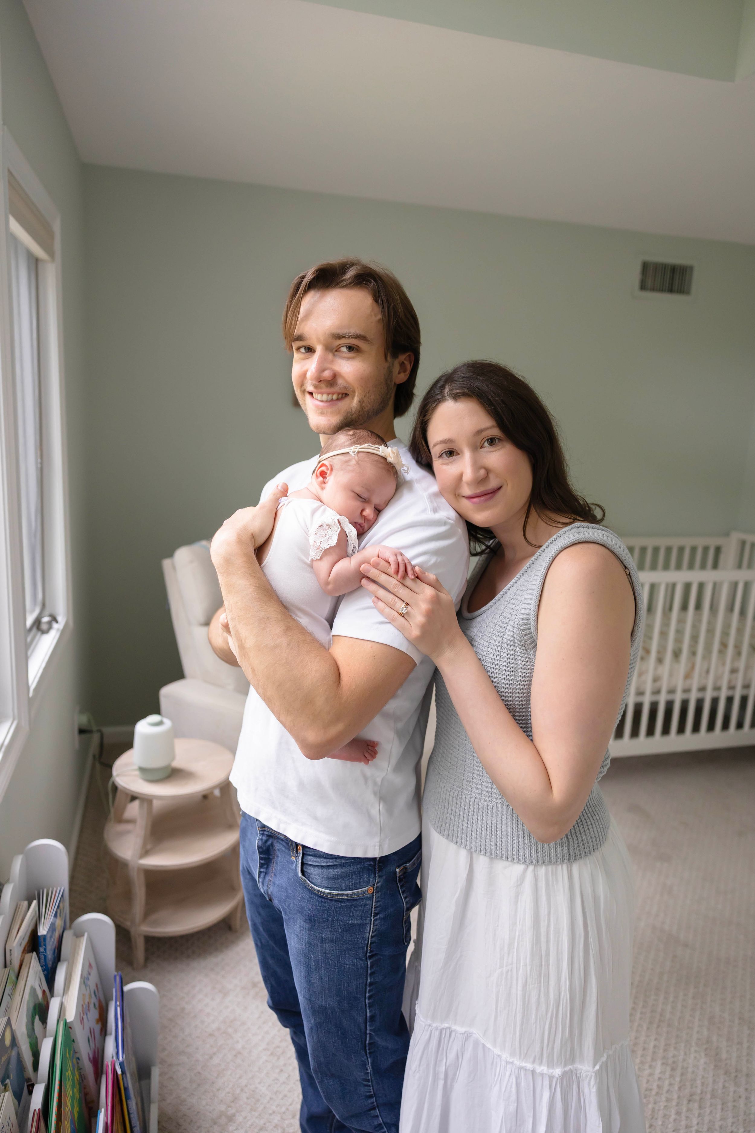 Young parents smiling and holding their newborn baby in a softly decorated nursery room.