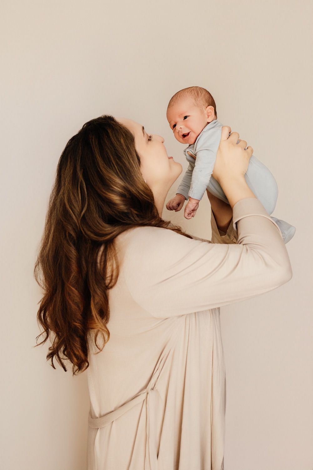 A mom holds her new baby in the air for a lifestyle portrait at their San Jose  in-home newborn photo session