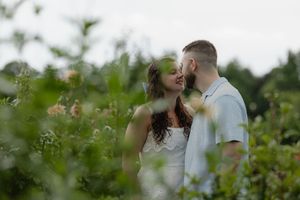 Couple sharing a romantic moment surrounded by lush green garden foliage and soft blooms outdoors.