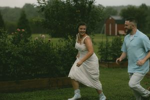 Laughing couple running through a green garden on a cloudy day, woman in white dress and man in blue shirt.