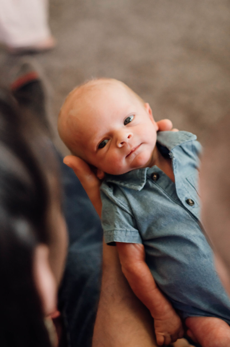Newborn baby peeks at camera from between parent's heads in a newborn photography session.