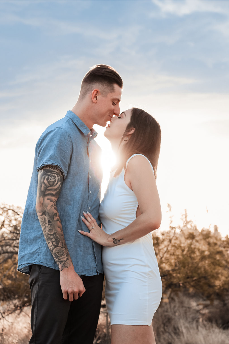 Couple exchanges kiss with sunset glow peeking from between them in Tucson Arizona desert couples engagement shoot.