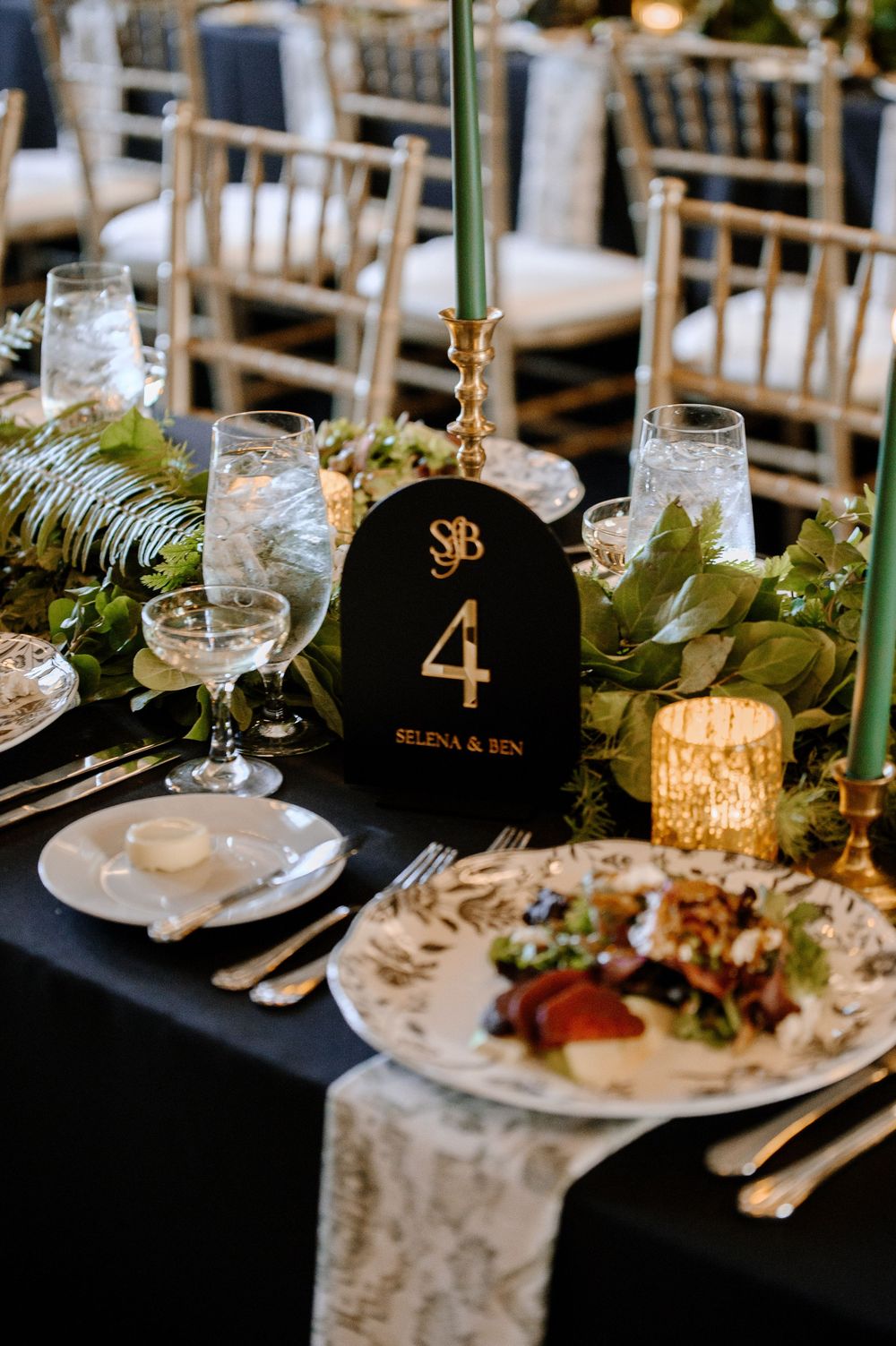 Elegant wedding table with black velvet number 4 sign, green candles, floral garland, and gold accents for Selena & Ben.