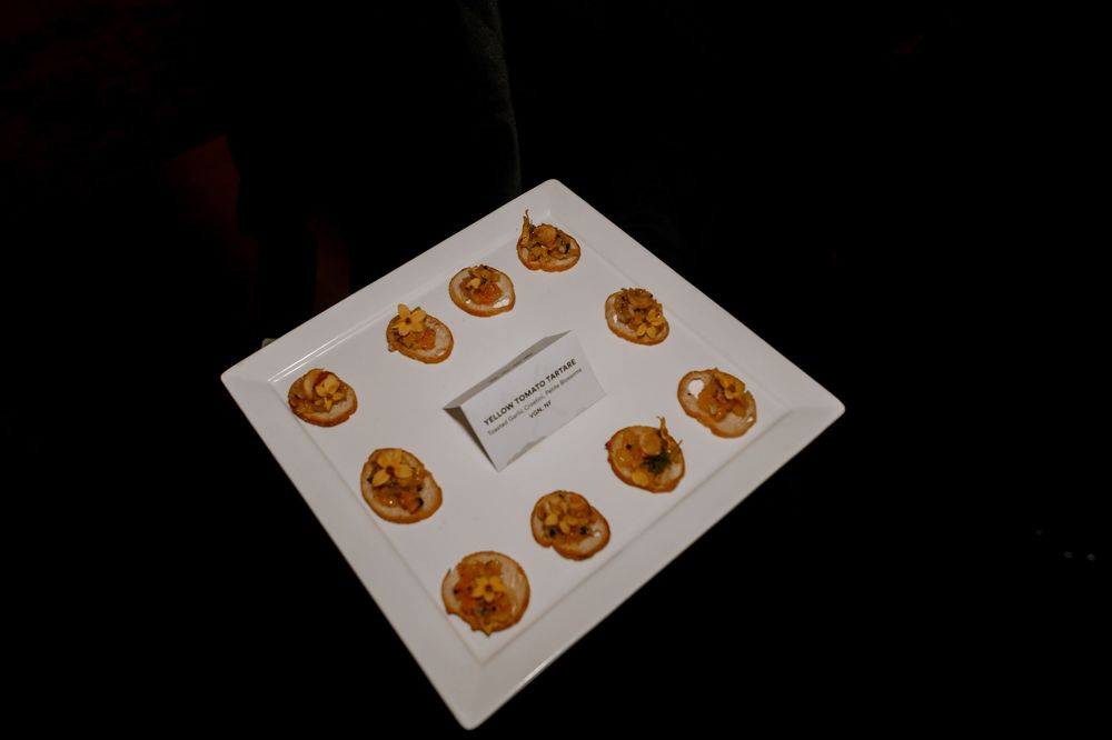 White tray displaying 10 elegant golden appetizer bites arranged symmetrically with a label card in the center.